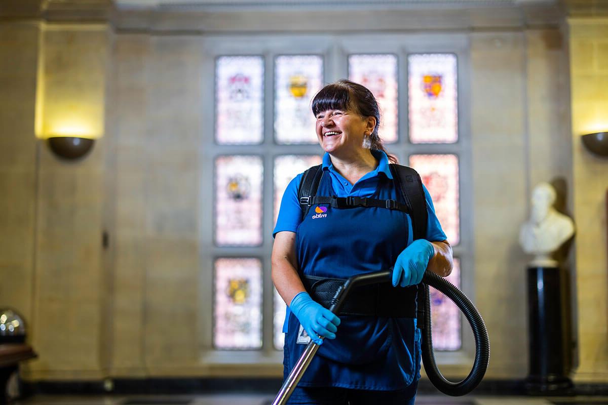 A Mitie female cleaning employee holding a vacuum cleaner in front of stained glass windows